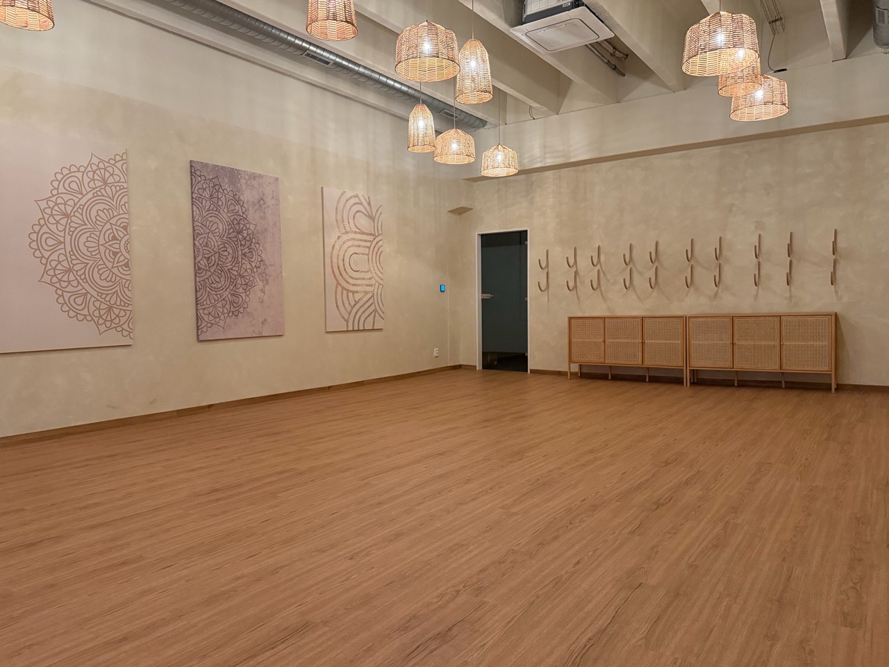 Dokončené jógové studio s obrazy, proutěnými lampami a dřevěnou podlahou